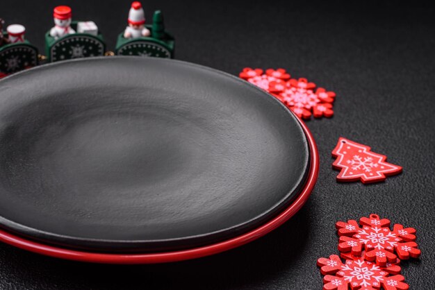 Пустая керамическая черная тарелка с элементами рождественского декора на праздничном текстурированном бетонном фоне