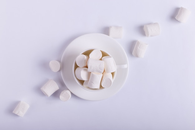 Empty ceramic cup with marshmallows on a saucer on white. Hard shadow from the sun, the concept of morning.