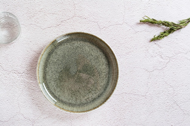 회색 배경에 있는 빈 세라믹 녹색 접시와 물 한 잔, 로즈마리 가지 상위 뷰 친환경 개념