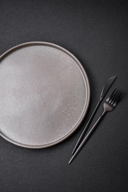 Empty ceramic plate on a dark textured background Preparing kitchen utensils for a family dinner