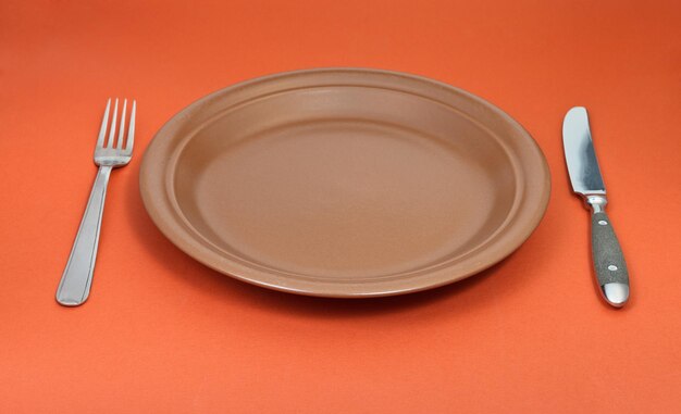 Empty ceramic plate with fork and knife on red