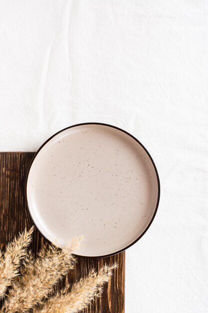 Empty ceramic plate on a wooden board on a cloth and dry ears Top view Ecofriendly concept