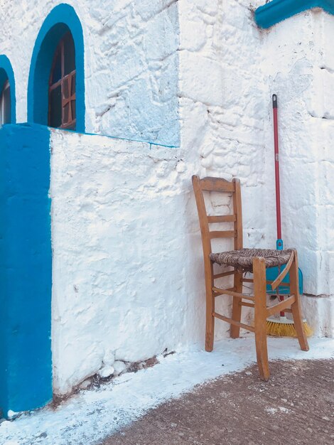 Empty chair and broom in front of white and blue building