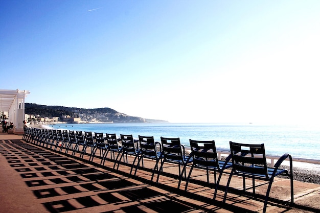 Empty chairs by railing at beach against sky