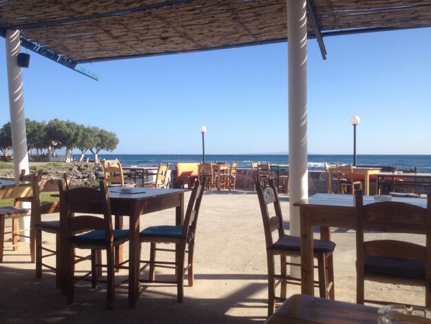 Empty chairs and tables at beach against clear sky