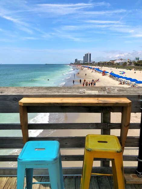 Empty chairs and tables on beach against sky