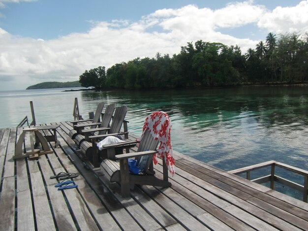 Empty chairs and tables by pier on island pier against sky