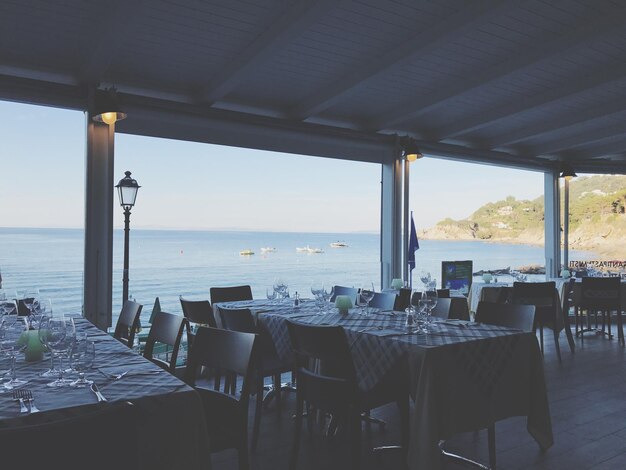 Foto sedie e tavoli vuoti in un ristorante sul mare contro il cielo