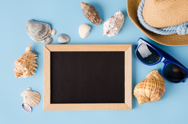 Empty chalkboard with seashells, hat and glasses.