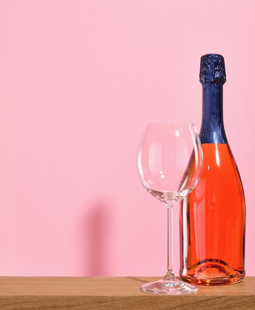 A empty champagne or wine glass a red bottle of alcoholic beverage on a pink background Copy space for text