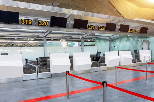 Foto banchi vuoti per il check-in per il deposito bagagli con percorsi annullati con un nastro rosso per differenziare i passeggeri al terminal dell'aeroporto.