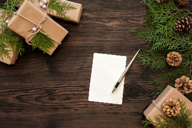 Empty Christmas card, gifts boxes, branch and fir cones on wood