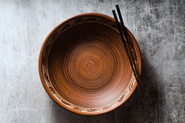 Empty clay plate and chopsticks on dark stone.