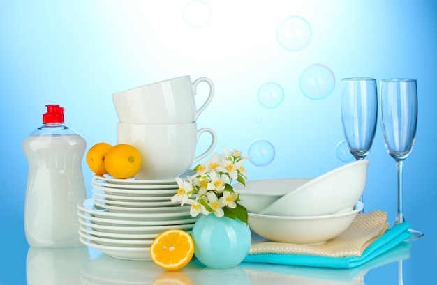 Photo empty clean plates glasses and cups with dishwashing liquid and lemon on blue background