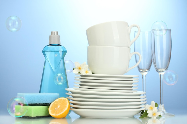 Photo empty clean plates glasses and cups with dishwashing liquid sponges and lemon on blue background