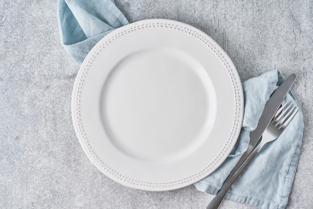 Empty clean white circle plate on grey linen tablecloth background with silverware