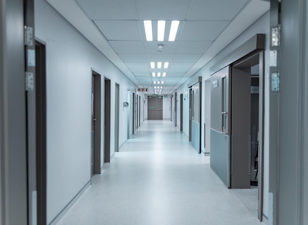 Пустой, чистый белый коридор в современной больнице с верхним освещением, выложенный дверями