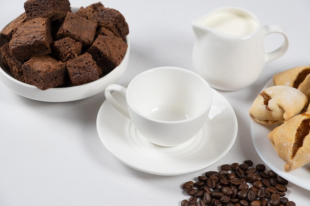 Tazza di caffè vuota in ceramica con brocca di latte torta al cioccolato e chicchi di caffè