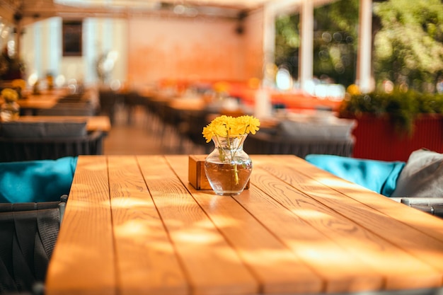 Empty cozy restaurant summer terrace with tables, chairs and yellow flowers in a glass vase in summer