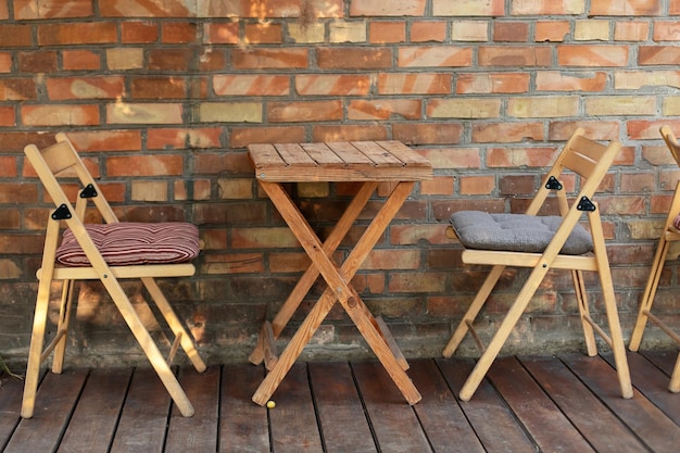 Svuota la caffetteria di strada accogliente con terrazza, sedia in legno, tavolo e muro di mattoni.