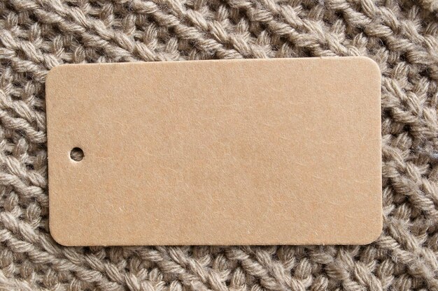 Empty craft paper clothing label on beige knit background closeup