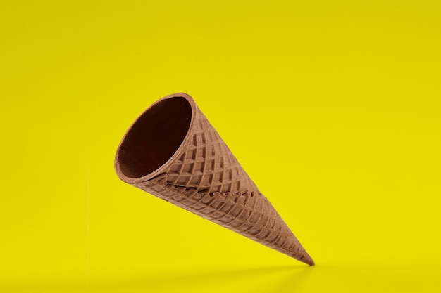 Empty crispy wafer cone for ice cream against yellow background concept of food treats mockup templa