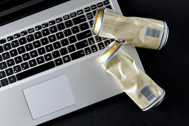 Empty crushed cans of beer on a laptop keyboard on a black background Drunken fights on social media