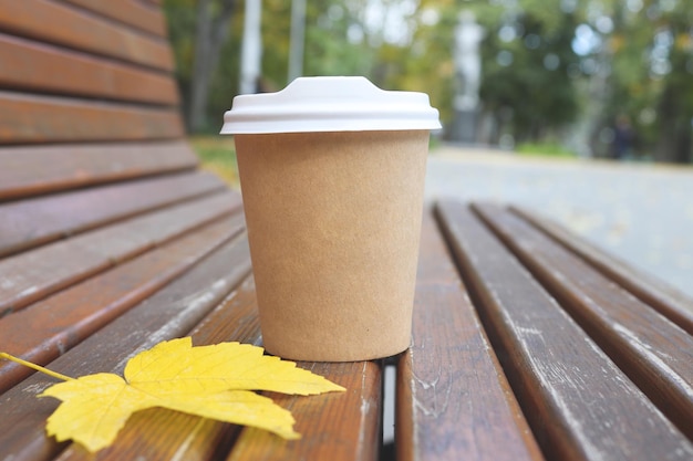 Empty cup of coffee and yellow leaf on bench against background of blurred autumn park Copy space