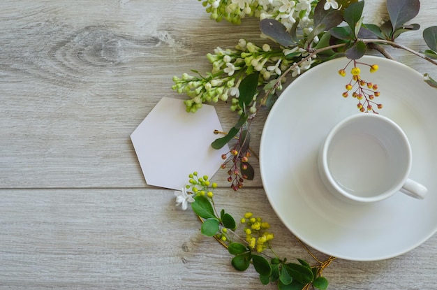 Empty cup on a saucer with mockup an empty white card framed by branches of green