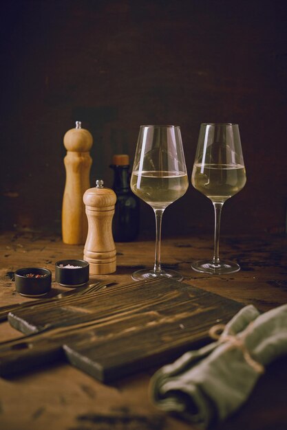 Empty cutting board two glasses of wine spice grinders and napkin on dark background