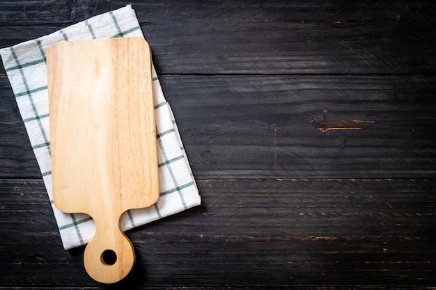 Tavola di legno di taglio vuota con panno da cucina su sfondo scuro
