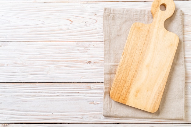 empty cutting wooden board with kitchen cloth on wooden background, top view