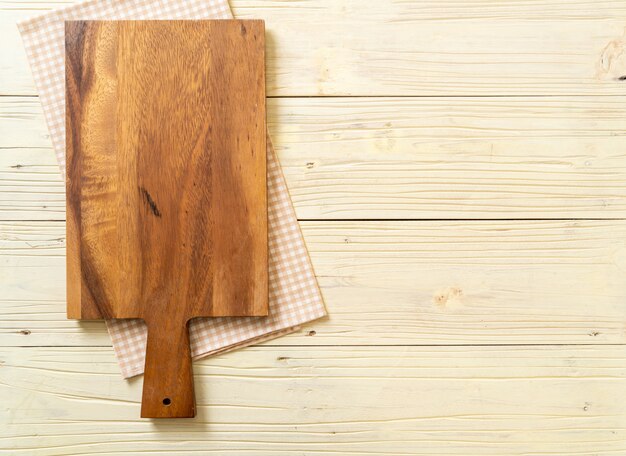 empty cutting wooden board with kitchen cloth on wooden background, top view