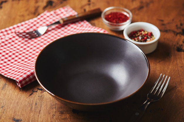 Empty dark bowl with fork napkin and spices on wooden background