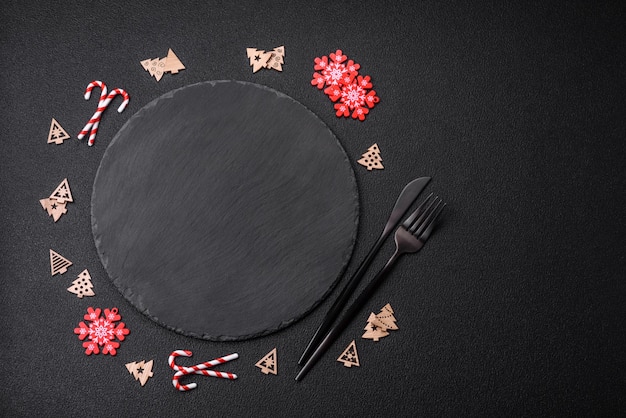 Empty dark ceramic plate with elements of Christmas decorations on a dark concrete background