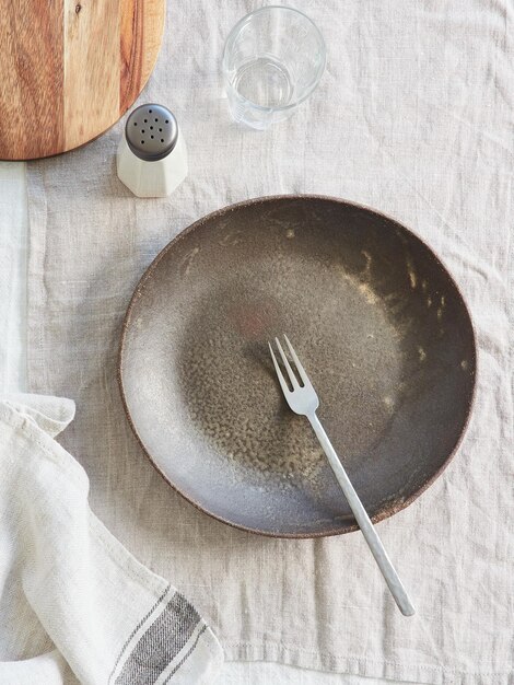 empty dark ceramic plate with fork napkin crystal glass salt shaker and wooden cutting board on the table on gray linen tablecloth