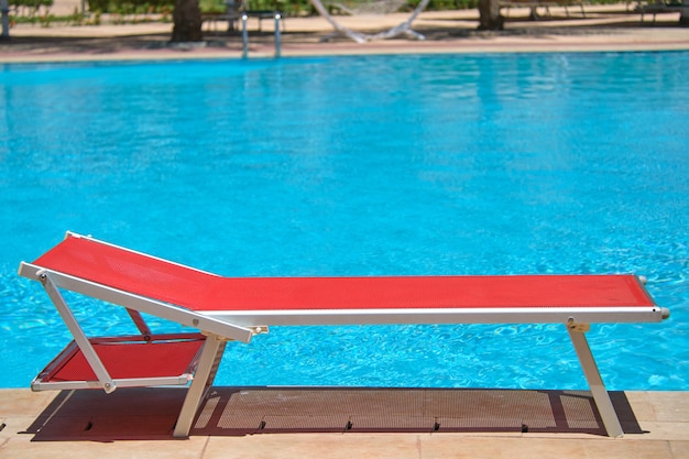 Empty deck chair on swimming pool side in summer resort. Vacations and getaway concept.