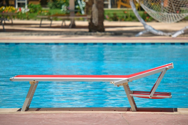 Empty deck chair on swimming pool side in summer resort. Vacations and getaway concept.