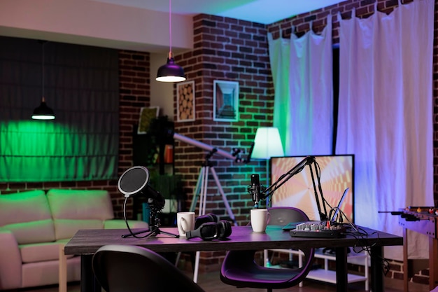 Empty desk in home production studio with podcast equipment technology recording sound for social media channel production. Live broadcasting space in living room with neon lights