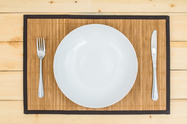 Empty dish with fork and knife on wooden table.