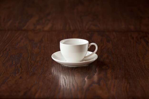 Svuoti la tazza bianca elegante sulla tavola di legno scura