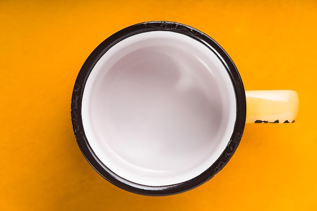 Empty enameled cup on the yellow background