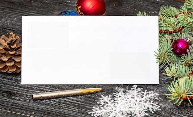 Empty envelope with pen, christmas decorations and branch of\
christmas tree on wooden table. new year postcard.