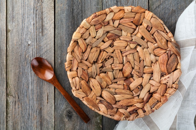 Empty flat plate made of rattan, wooden spoon and linen napkin on an old rustic surface. Top view. Selective focus.