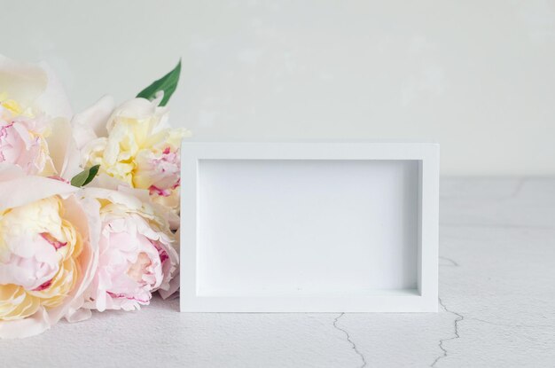 Empty frame and bouquet of white peonies on grey background