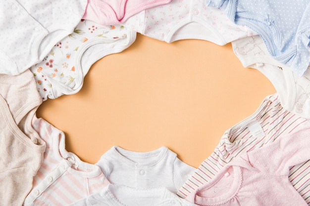 Photo an empty frame made with baby's clothing on an orange backdrop