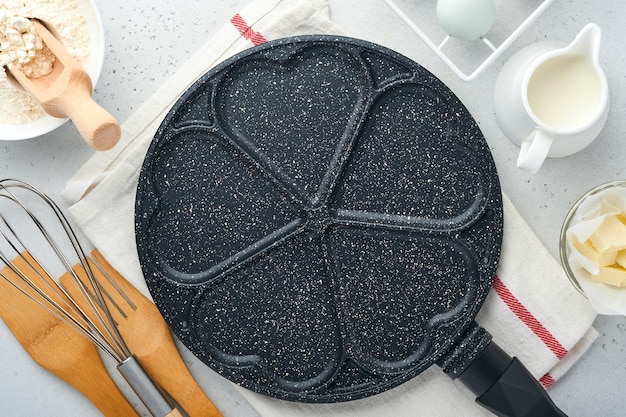 사진 검은색 빈 프라이팬, 석재 논스틱 코팅이 된 프라이팬은 아침 식사 하트 모양으로 팬케이크를 굽고 회색 콘크리트 테이블 배경에 재료를 넣습니다. 발렌타인 데이를 위한 아침 식사. 평면도.