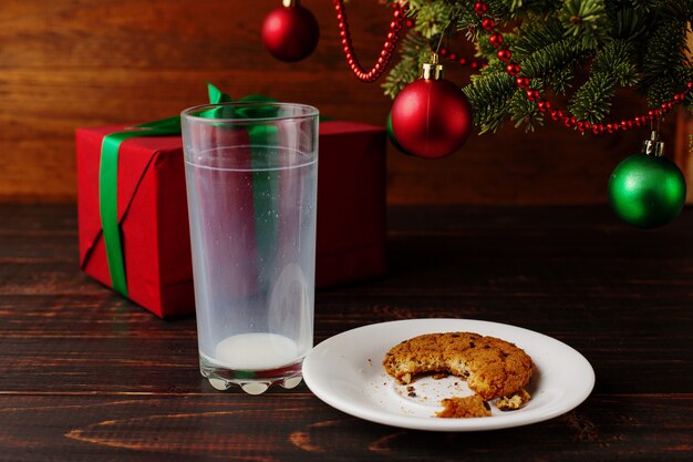 Biscotti vuoti del bicchiere di latte e della briciola e un regalo sotto l'albero di natale. l'arrivo di babbo natale.