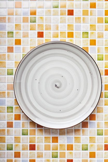 Empty gray plate on background of multicolored small mosaics