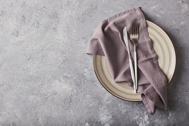 Empty gray plate with napkin and cutlery on gray background